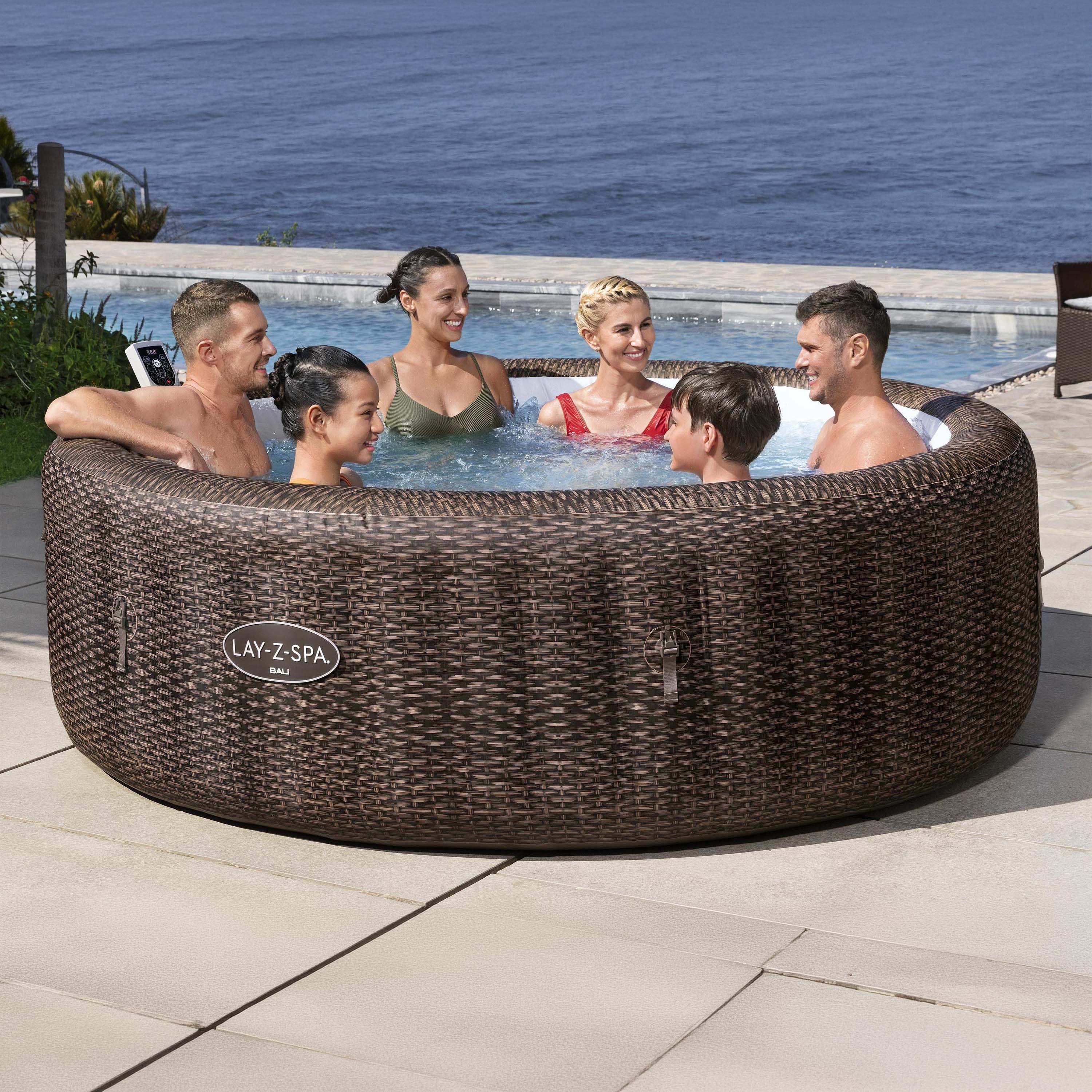 Nafukovacie jacuzzi LAY-Z-SPA® BALI SMART AIRJET™ v hnedom ratanovom prevedení s ľuďmi na terase pri mori