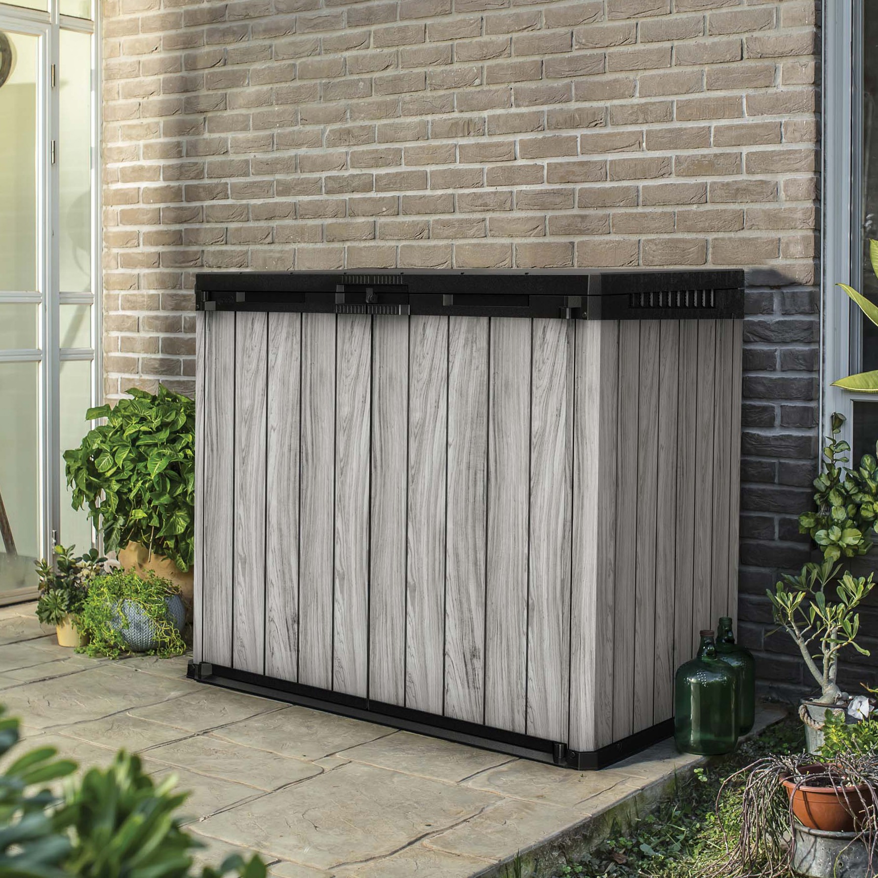 Záhradný organizér Keter SIO Darwin 1150L Storm Grey umiestnený na terase pri tehlovej stene