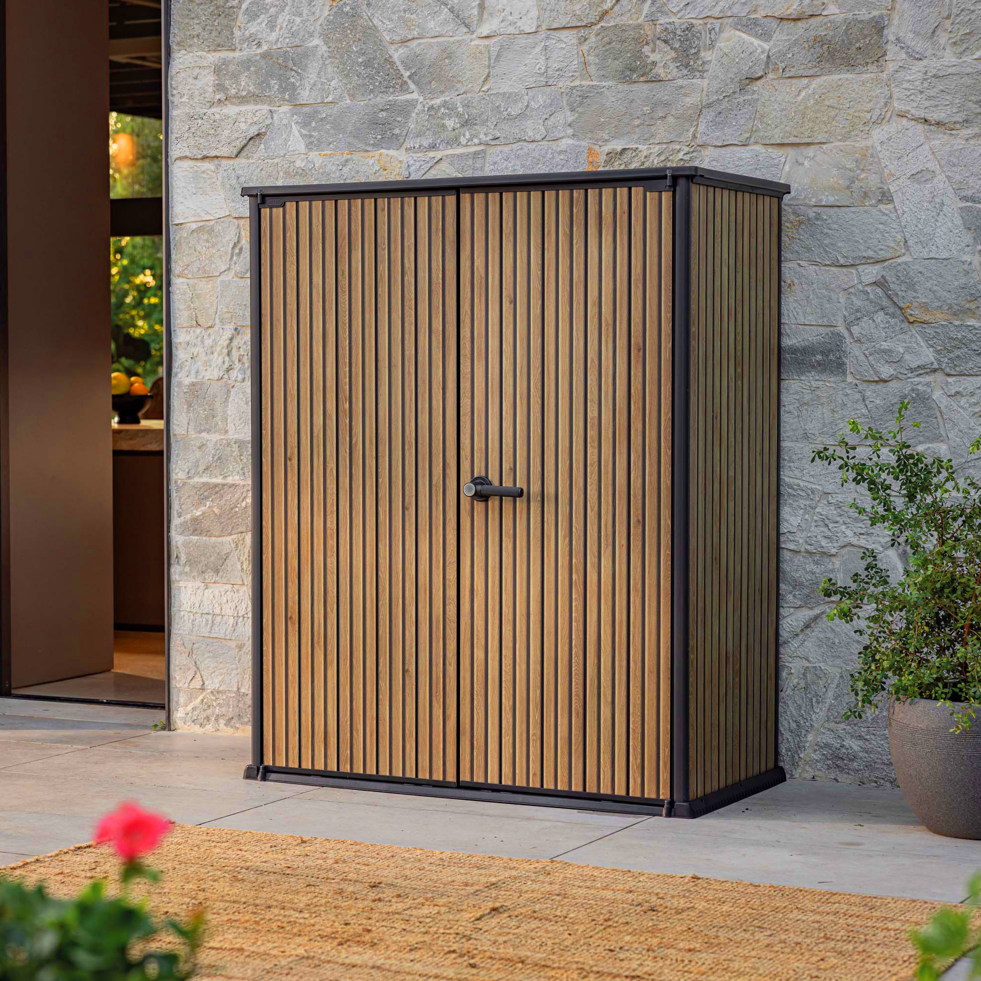 Záhradný box Keter Deco Vertical 1400L Venetian Brown s dvojkrídlovými dverami na terase pri kamennom múre