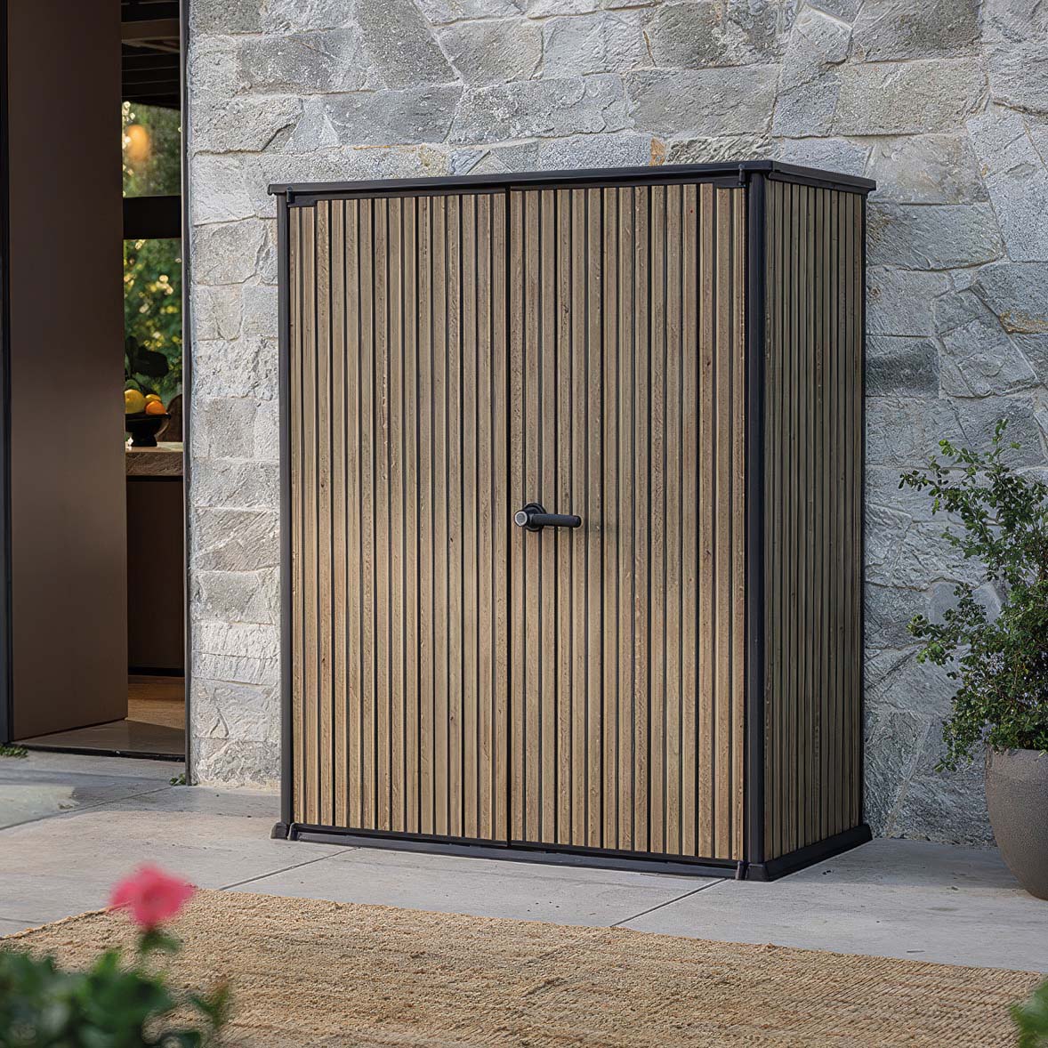 Záhradný box Keter Deco Vertical 1400L Venetian Brown s dvojkrídlovými dverami na terase pri kamennom múre