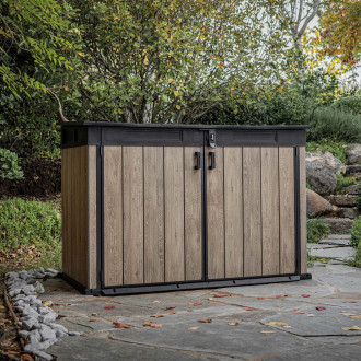 Záhradná skriňa Keter Deco Horizontal 2020L Ashwood s čiernym rámom umiestnená v záhradnom prostredí na kamennej dlažbe