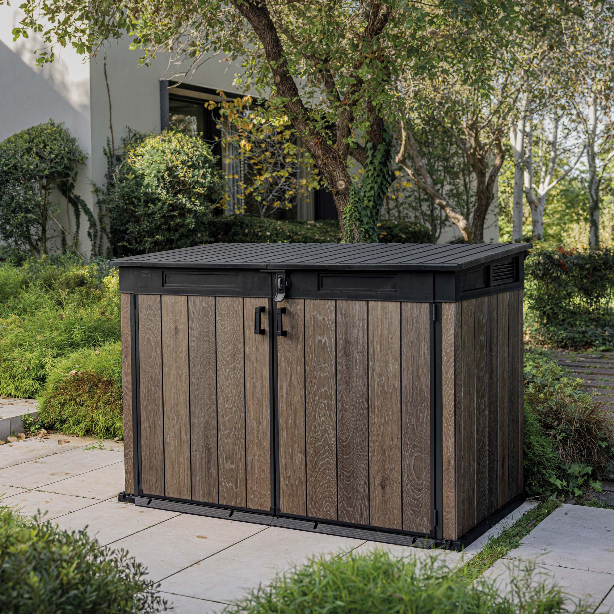 Záhradná skriňa Keter Deco Horizontal 2020l Walnut v hnedej farbe s čiernym rámom umiestnená v záhrade na dlažbe