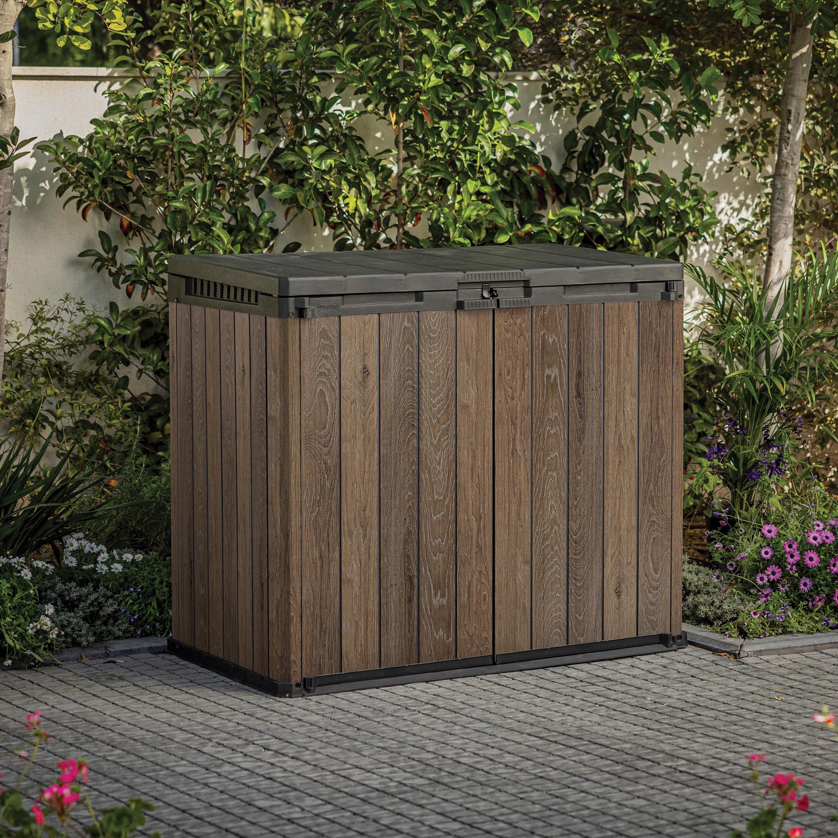 Záhradný box Keter Darwin 1150l Walnut v hnedej farbe s imitáciou dreva, umiestnený v záhrade na dlažbe