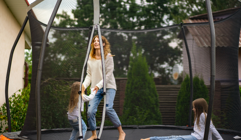 kobieta skacząca z c&oacute;rkami na trampolinie ogrodowej 