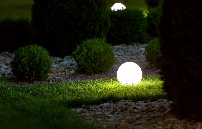Z&aacute;hradn&aacute; lampa v tvare gule umiestnen&aacute; na tr&aacute;ve vedľa zelen&eacute;ho kvetinov&eacute;ho z&aacute;honu