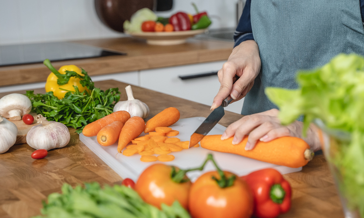 Dom&aacute;ca gazdinka kr&aacute;ja mrkvu na pr&iacute;pravu ingredienci&iacute; do &scaron;al&aacute;tu na obed v kuchyni