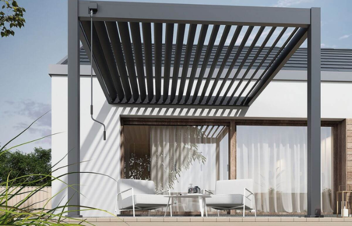 čierna z&aacute;hradn&aacute; pergola s pohybliv&yacute;mi lamelami na streche ako relaxačn&aacute; z&oacute;na na terase so z&aacute;hradn&yacute;m n&aacute;bytkom