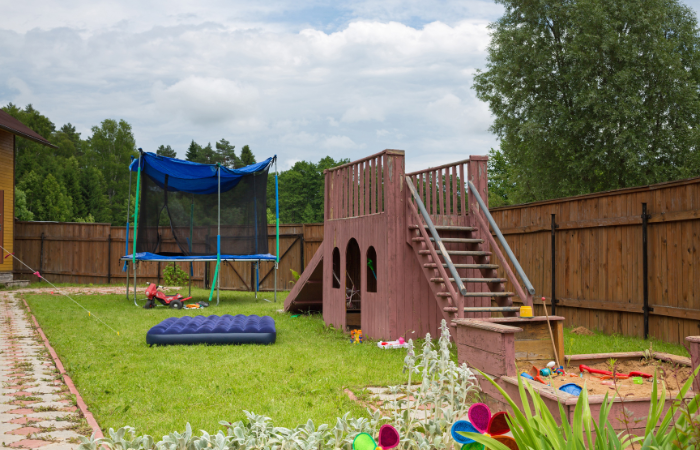 trampolina ogrodowa dla dzieci ustawiona w ogrodzie obok placu zabaw i piaskownicy